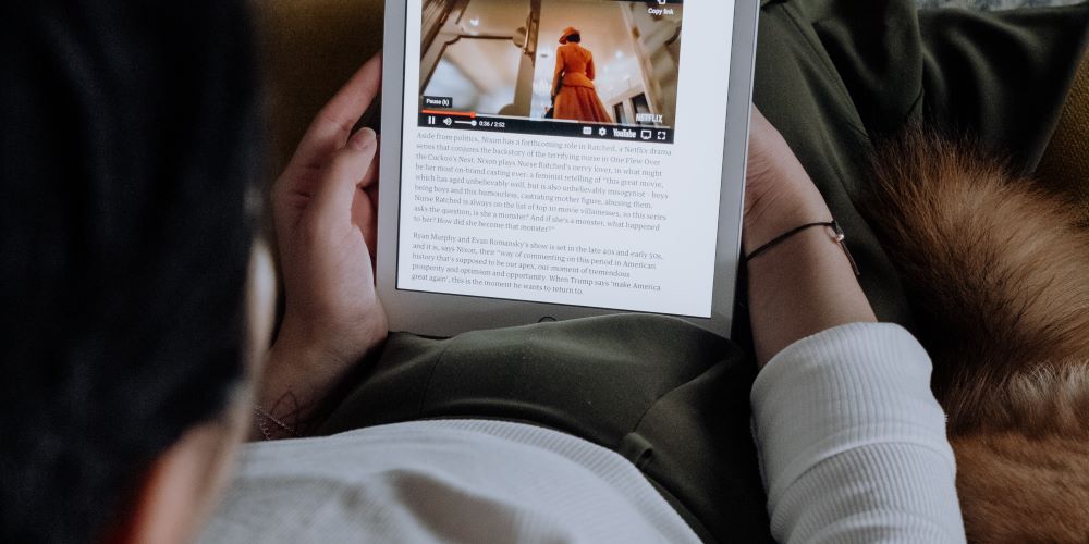 Zeigt Person mit Tablet auf den Oberschenkeln am Lesen.
