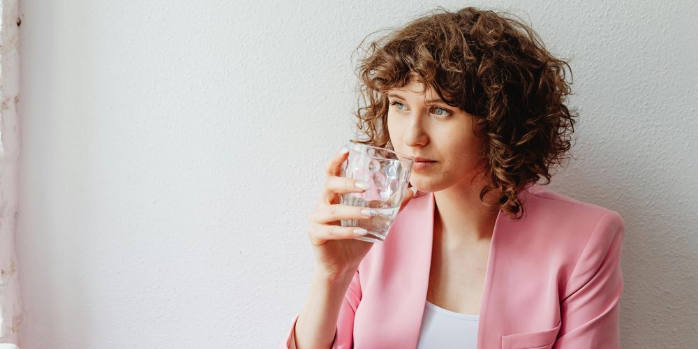 Frau trinkt ein Glas voll Wasser vor jeder Mahlzeit zum Abnehmen. Hilft das wirklich?