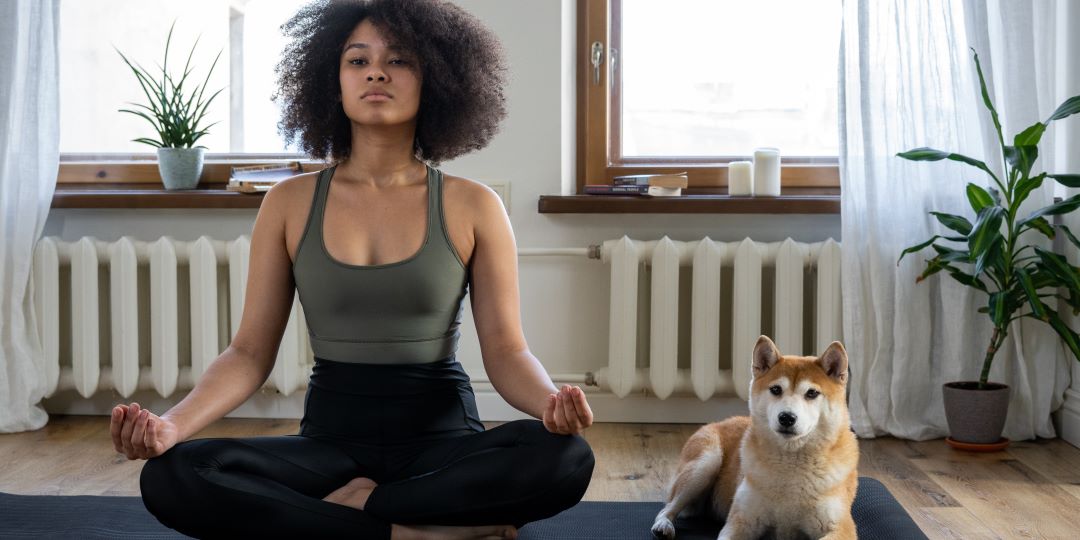 Frau im Schneidersitz mit Hund auf Yogamatte