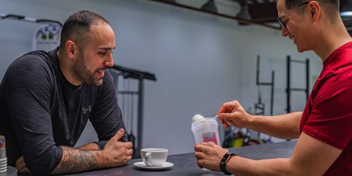 Zwei Sportler mixen High-Protein Pulver in Shake für ihren Muskelaufbau