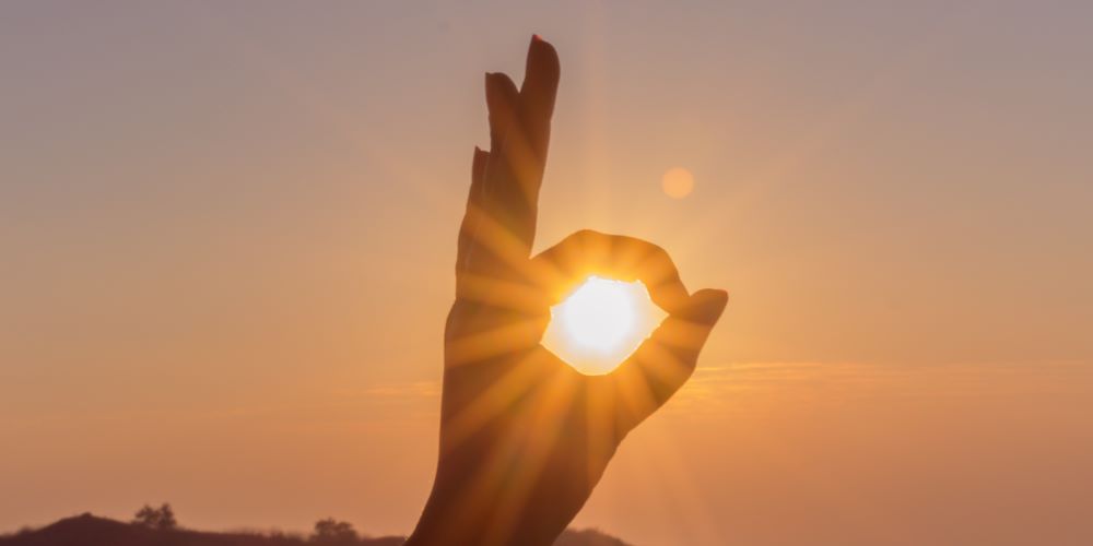 Untergehende Sonne scheint durch Kreis aus Zeigefinger und Daumen.