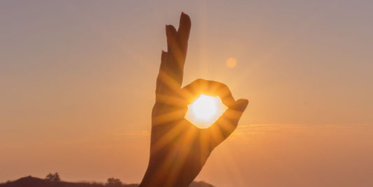 Untergehende Sonne scheint durch Kreis aus Zeigefinger und Daumen.