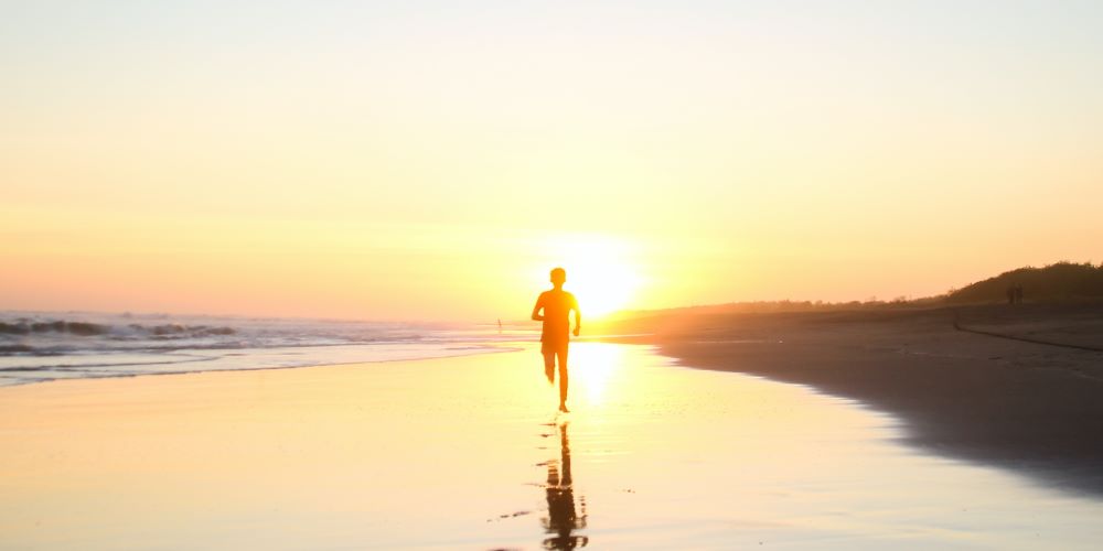 Läufer joggt im Gegenlicht des Sonnenuntergangs am Strand