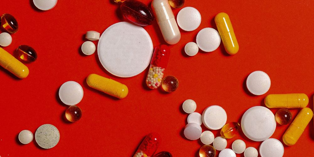 Viele verschiedene Tabletten/Kapseln liegen auf roten Untergrund