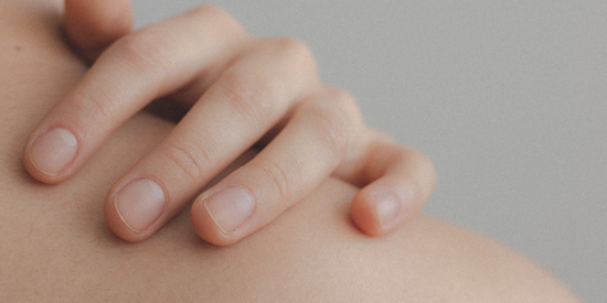 Zeigt eine Hand auf der nackten Schulter mit Fokus auf Fingernägel